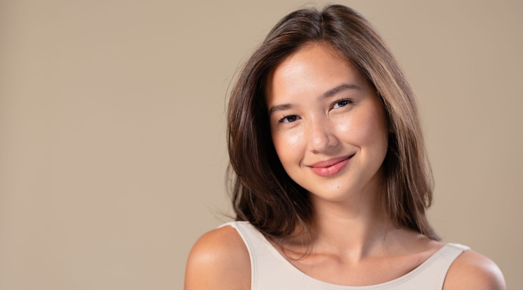 Smiling young woman with long brown hair against a beige background